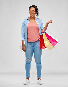 零售摄影照片_销售和出口概念—快乐的非洲裔美国年轻妇女有购物袋在灰色背景快乐的非洲裔美国妇女与购物袋