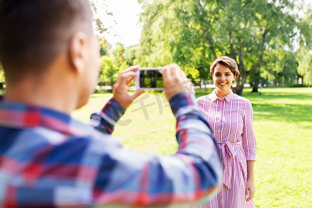 人，技术和生活方式的概念—快乐的夫妇拍摄智能手机在夏季公园。夫妇拍摄通过智能手机在公园