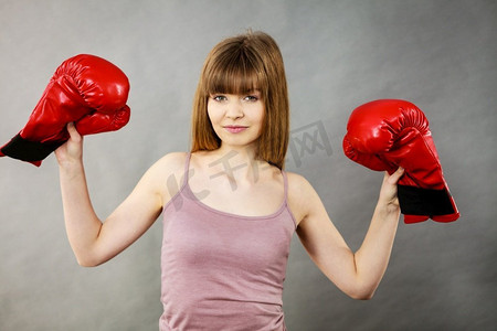 运动女子拿着红色拳击手套，战斗。工作室拍摄灰色，背景。妇女拿着拳击手套
