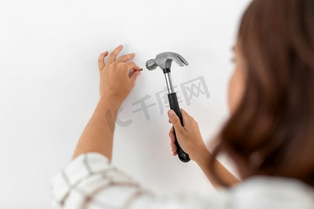 家庭改善，修理和人的概念—妇女近摄锤钉子到墙上。关闭的妇女锤钉到墙上在家里