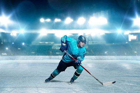 戴头盔摄影照片_一个曲棍球运动员滑冰与棒在冰竞技场，聚光灯背景。戴头盔、手套和制服的男子玩游戏