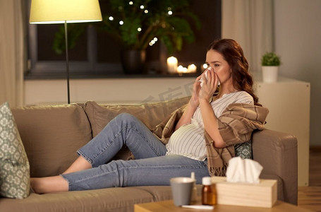孕妇生病摄影照片_怀孕和人的概念—生病的孕妇在家里用纸巾擤鼻涕。生病的孕妇在家里擤鼻涕