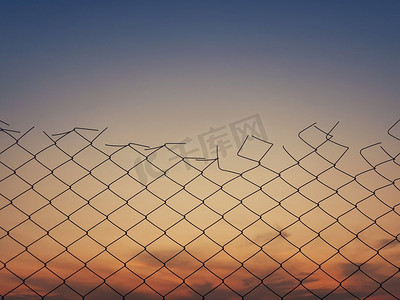 天空围栏摄影照片_老铁丝网栅栏纹理反对日落天空背景。