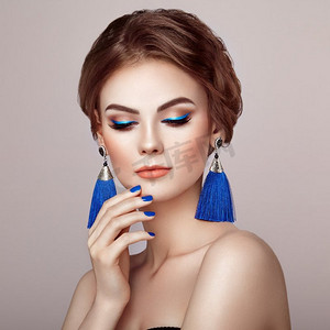 美丽的女人与大耳环流苏珠宝蓝色颜色。完美的化妆和优雅的发型。蓝色化妆箭头蓝指甲美甲