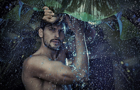 英俊的男人凝视着热带的雨