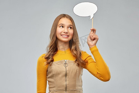 沟通和人的概念—微笑的少女拿着空白的讲话气泡在灰色背景。十几岁的女孩拿着讲话泡沫