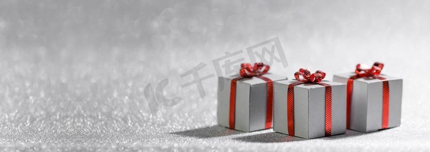 生日小卡片摄影照片_小装饰性圣诞礼盒与银色闪闪发光的背景与复制空间的红色丝带蝴蝶结。圣诞礼品盒