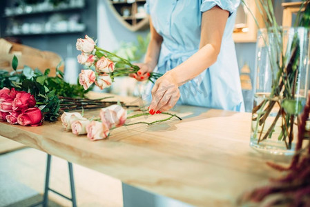 女花商在花店的桌子上使玫瑰组成。花艺艺术家在工作场所制作花束