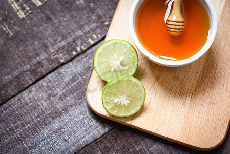 切菜板上的蜂蜜柠檬酸橙和杯中的蜂蜜，深色木质背景