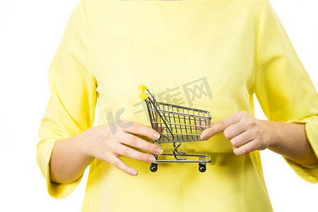 零售摄影照片_在市场购物的概念。快乐微笑的女人手拿着小小的购物车手推车。妇女拿着小购物车