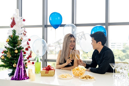 一对年轻的亚洲成年夫妇在大城市大公寓的客厅里一起喝着汽酒庆祝新年圣诞假期