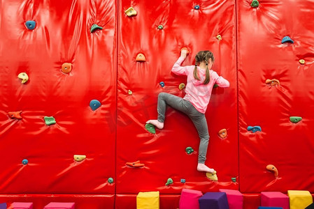 女孩爬在一个墙壁在儿童游乐场。娱乐中心。快乐的童年