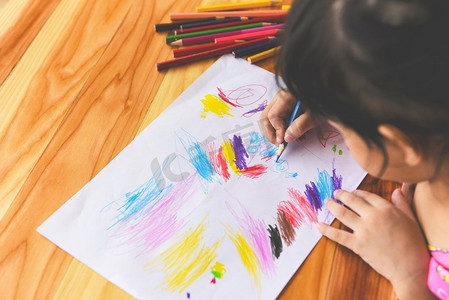 女儿图片摄影照片_女孩绘画在纸上与彩色铅笔在家里的木桌/做绘画图片和五颜六色的蜡笔的孩子