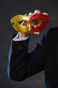 节日，人和庆祝的概念。男性手持红色金色狂欢节面具特写在黑暗。男性手持狂欢节面具特写镜头