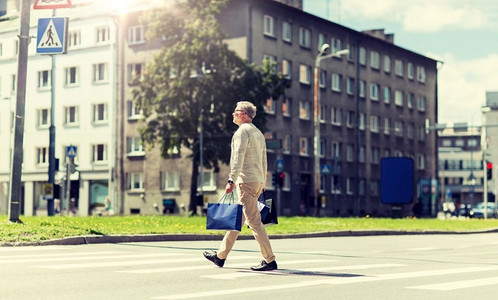 销售，交通和人的概念—老年男子购物袋走在城市人行横道。带着购物袋的老年男子走在人行横道上