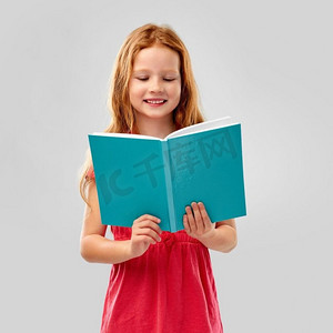 红发摄影照片_童年与人的概念-微笑的红发女孩在灰色背景下阅读书籍。微笑的红发女孩看书