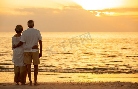 高级男女夫妇拥抱在日落或日出在一个废弃的热带海滩 