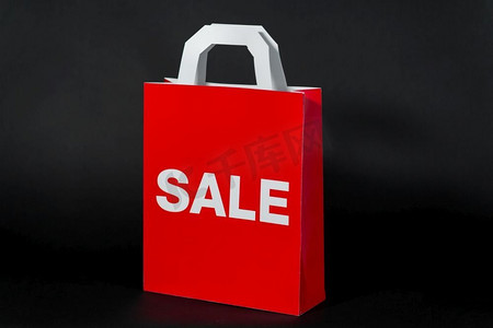 销售、消费主义和奥特莱斯理念--手持黑色背景的红色购物袋。印有促销字样的红色购物袋