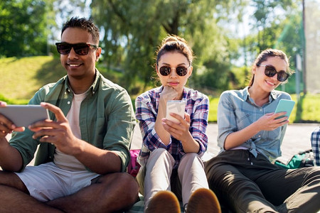 手机夏季夏季摄影照片_友谊，技术和旅行概念—一群朋友在夏季公园的智能手机。朋友在夏季公园的智能手机