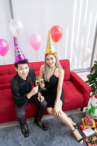 年轻的亚洲成人夫妇庆祝新年圣诞假期与起泡葡萄酒一起在大公寓的客厅在大城市
