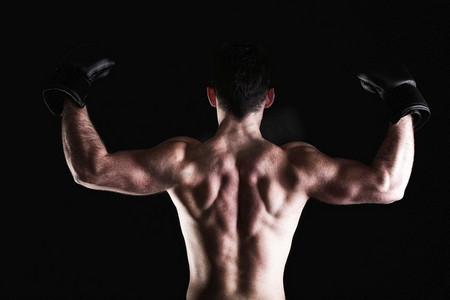 拳击手提高他的手臂强壮的运动肌肉人，运动家伙显示他的肌肉男性背部孤立在黑色背景