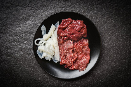 套肉牛肉片和肝脏在黑板熟的或寿喜烧涮锅的黑暗背景日本食品亚洲菜/新鲜牛肉生 