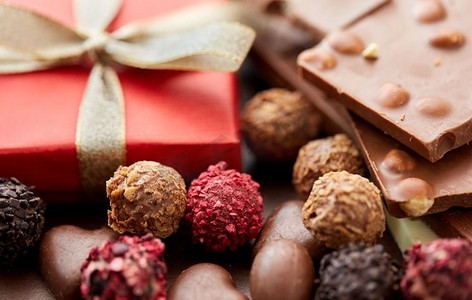 草莓夹心黑巧克力摄影照片_糖果概念—手工巧克力糖果和红色礼品盒特写镜头。手工巧克力糖果特写