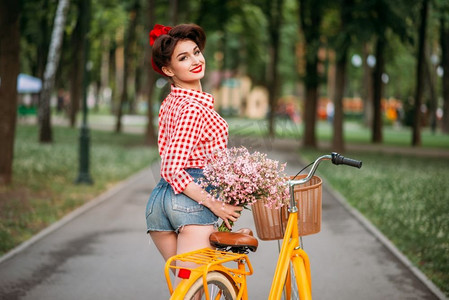 骑着复古自行车和花束的美女。靓丽的美女。骑着复古自行车，背着花束的美女