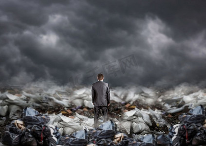 商人站在垃圾填埋场的中间，背影，一堆堆垃圾。环境企业与生态污染问题