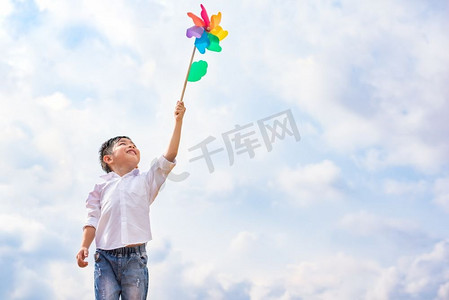 男孩在户外大风中手持五颜六色的风车。儿童肖像和儿童主题游戏。