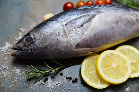 新鲜的鱼与香草香料迷迭香番茄和柠檬/生鱼海鲜在黑色板背景，长尾金枪鱼，东部小金枪鱼