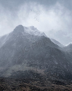 风景山摄影照片_令人惊叹的情绪戏剧性冬季风景山的图像被白雪覆盖的Y Garn在Snowdonia与鸟飞行高以上