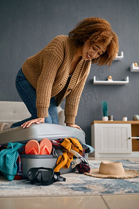 一名女子试图合上超载的行李箱，推着盖子。为度假旅游做准备。一名女子试图关闭超载的旅行箱