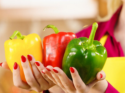 女子手持甜椒，美味健康的节食蔬菜，呈现三种颜色的减肥食品。拿着甜椒和辣椒粉的女人
