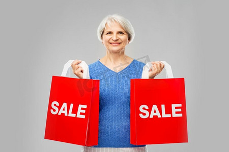 销售和老人概念—微笑的高级妇女有购物袋在灰色背景。老年妇女与购物袋超过灰色