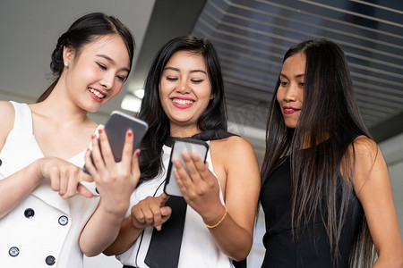 三个女性朋友正在交谈，而看着他们手中的手机。社交媒体、八卦新闻和网上购物的概念。