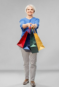 零售摄影照片_销售和老人概念—微笑的高级妇女眼镜与购物袋在灰色背景老年妇女与购物袋超过灰色