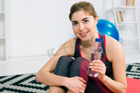 塑料水瓶摄影照片_肖像快乐的年轻女子拿着塑料水瓶