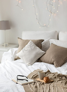 卧室毛毯摄影照片_舒适、卫生和室内概念-咖啡、牛角面包、毯子和书籍在舒适的家中躺在床上。家里的床上有咖啡、牛角面包、毯子和书
