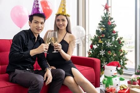 一对年轻的亚洲成年夫妇在大城市大公寓的客厅里一起喝着汽酒庆祝新年圣诞假期