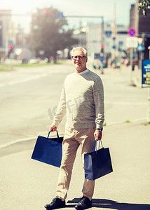 销售，消费主义和人的观念—老年人带着购物袋走在城市里。带着购物袋的老年男子在城市里行走