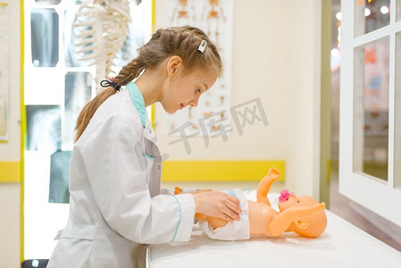 穿制服的小女孩玩医生与玩具娃娃，游戏室。孩子在假想医院扮演医务工作者，专业学习，幼稚的梦想