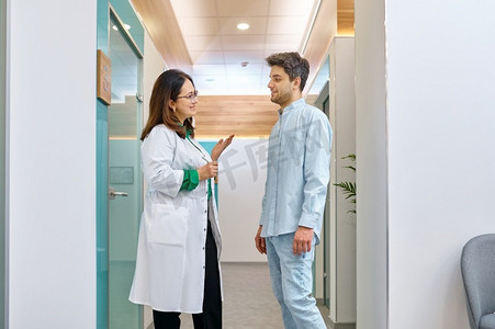 女医生和男病人谈话。医生在走廊里向年轻人解释什么。女医生与男病人讨论某事