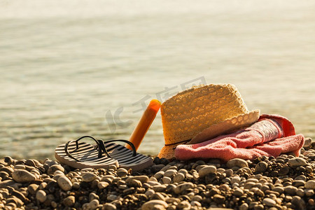 沙滩配件的毛巾日光浴。阳光明媚的帽子和人字拖，石头石头沙子。太阳帽和人字拖在石头海滩
