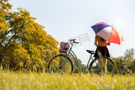 下雨热摄影照片_公园里打着凉伞、骑着自行车的女人。人与放松的概念。季节和秋天的主题。