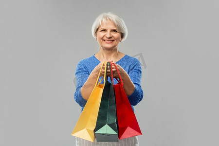 销售和老人概念—微笑的高级妇女眼镜与购物袋在灰色背景老年妇女与购物袋超过灰色