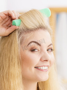卡通女卷发孩摄影照片_金发女郎女人使用卷发器来创建美丽的发型在她的发型。金发女郎女人使用卷发器
