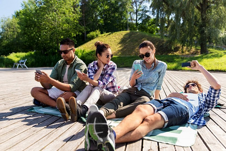 友谊，技术和旅行概念—一群朋友在夏季公园的智能手机。朋友在夏季公园的智能手机