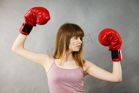 穿着红色拳击手套的运动女，正在打架。工作室拍摄灰色，背景。戴拳击手套的女人