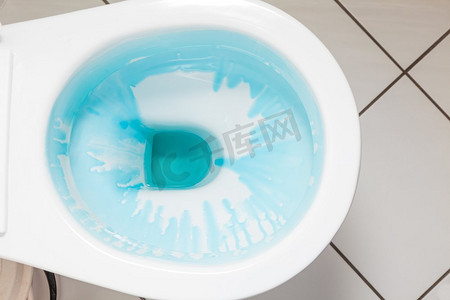洗涤剂摄影照片_清洁和消毒概念。白色马桶，冲洗后用蓝色洗涤剂。白色马桶，配蓝色洗涤剂